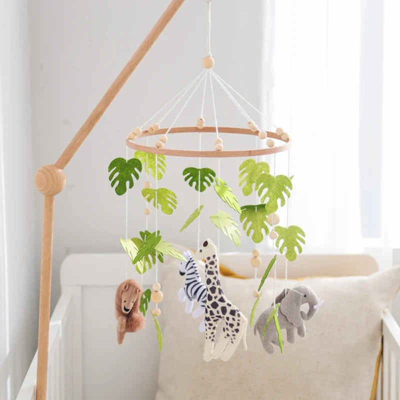 Wooden crib mobile with soft felt forest animals and green leaves hanging above a white baby crib