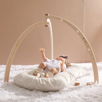 Foldable wooden baby play gym set with sensory rattle and hanging toys on a soft cushion for newborn sensory development.