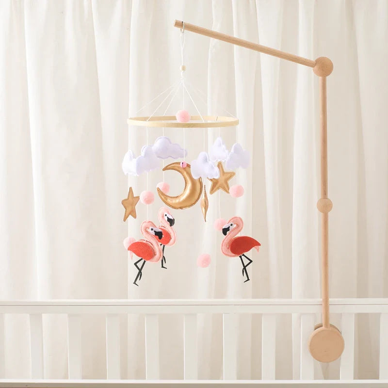 Wooden flamingo crib mobile with soft felt flamingo dolls, clouds, stars, and a crescent moon hanging above a white baby crib.