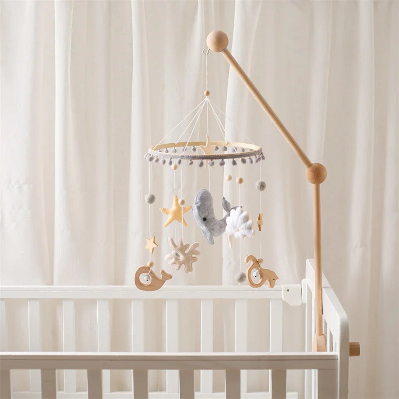 Wooden ocean-themed baby mobile rattle with hanging sea creatures and stars, attached to a white crib.