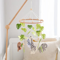 Wooden crib mobile with soft felt forest animals and green leaves hanging above a white baby crib