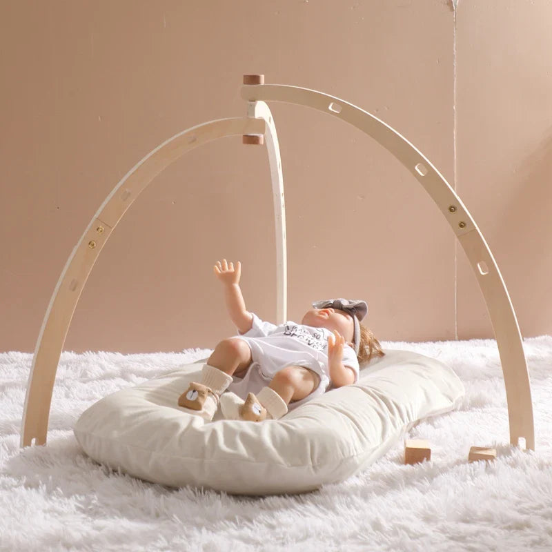 Foldable wooden baby play gym set with sensory rattle and hanging toys on a soft cushion for newborn sensory development.