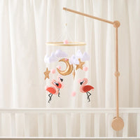 Wooden flamingo crib mobile with soft felt flamingo dolls, clouds, stars, and a crescent moon hanging above a white baby crib.