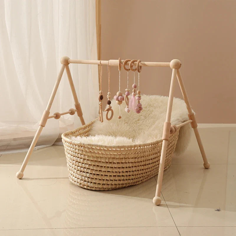 Minimalist baby wooden gym frame with hanging sensory rattle toys above a woven bassinet basket