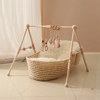 Minimalist baby wooden gym frame with hanging sensory rattle toys above a woven bassinet basket